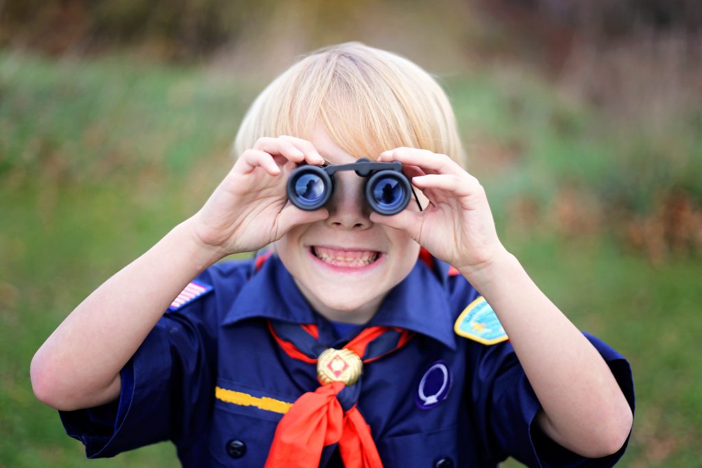 Cub scout in uniform looking through binoculars during scouting merit badge classes and workshops